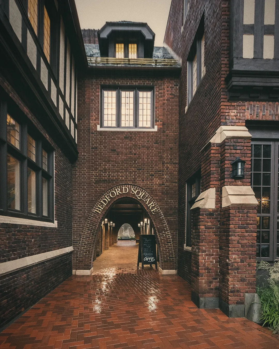 A brick Tudor archway over a wet courtyard