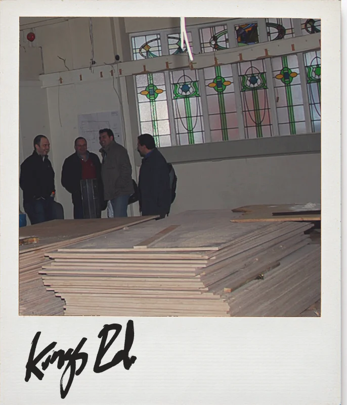 Photo, Anthropologie King’s Road, London, before the build: four people in the empty hall under the old stained-glass windows, timber stacked in front